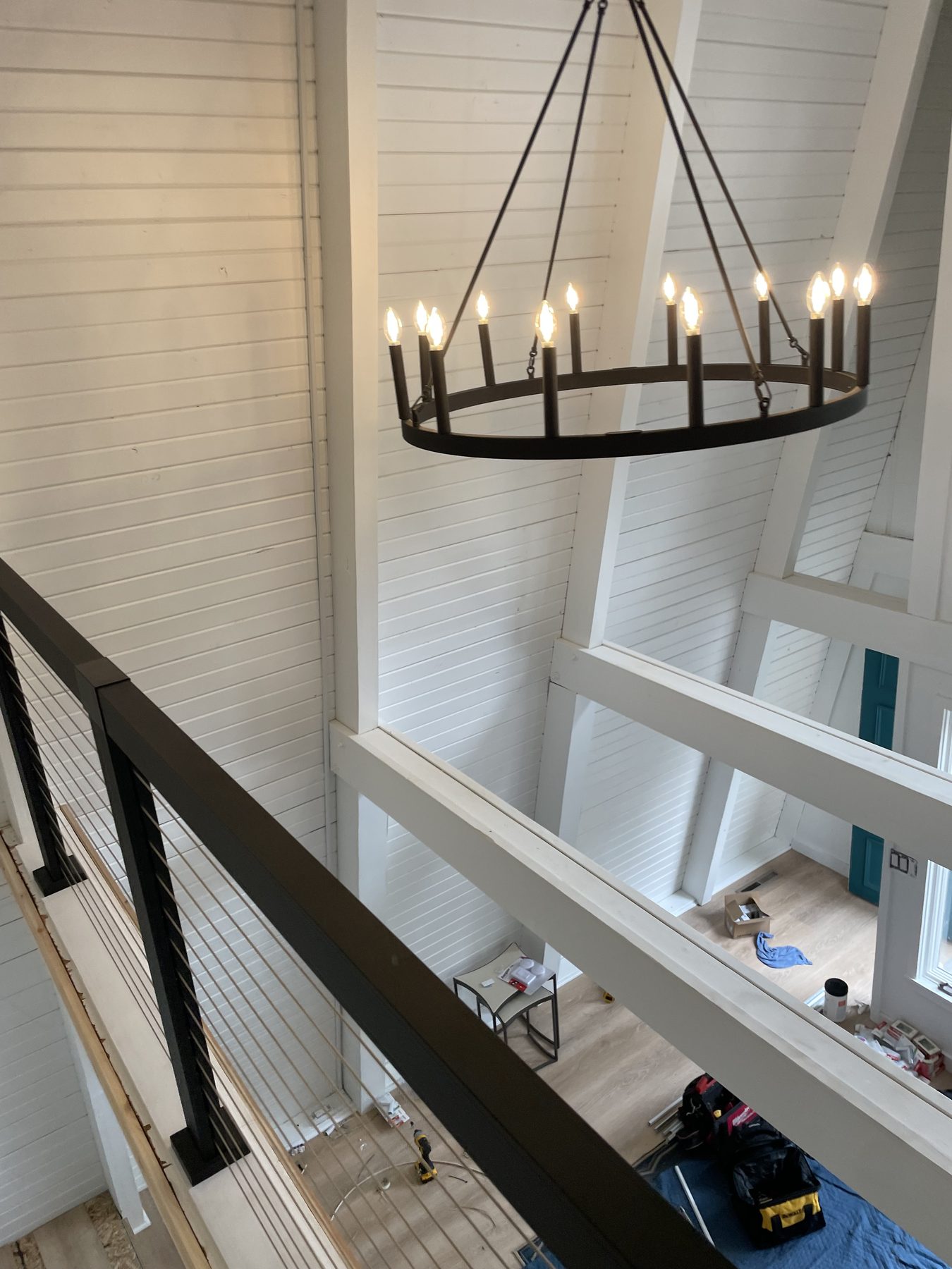 Iron candle-arm chandelier suspended in a tall vaulted white shiplap room with coffered ceiling beams and skylights