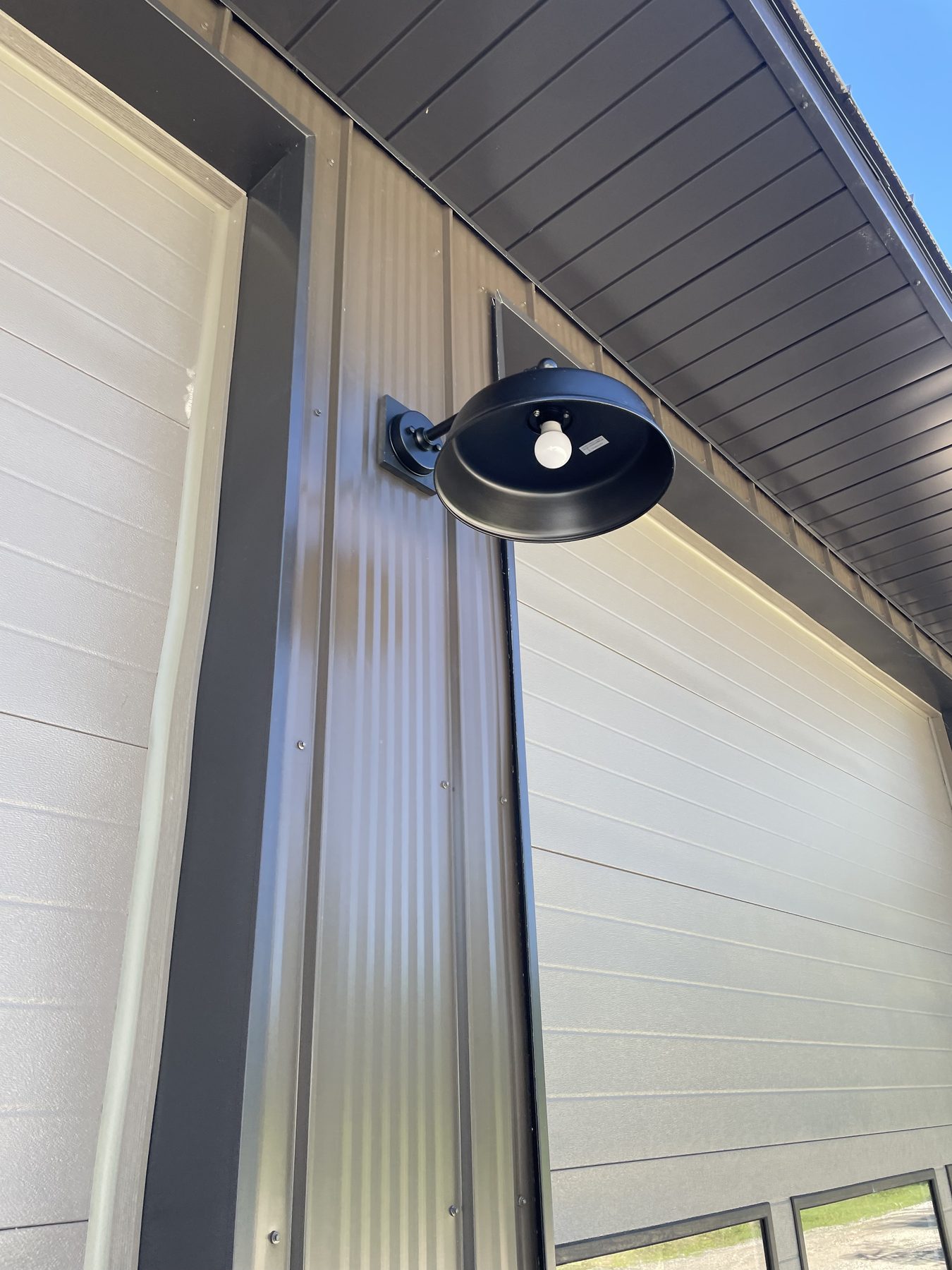 Black exterior wall sconce on dark vertical metal siding under blue sky
