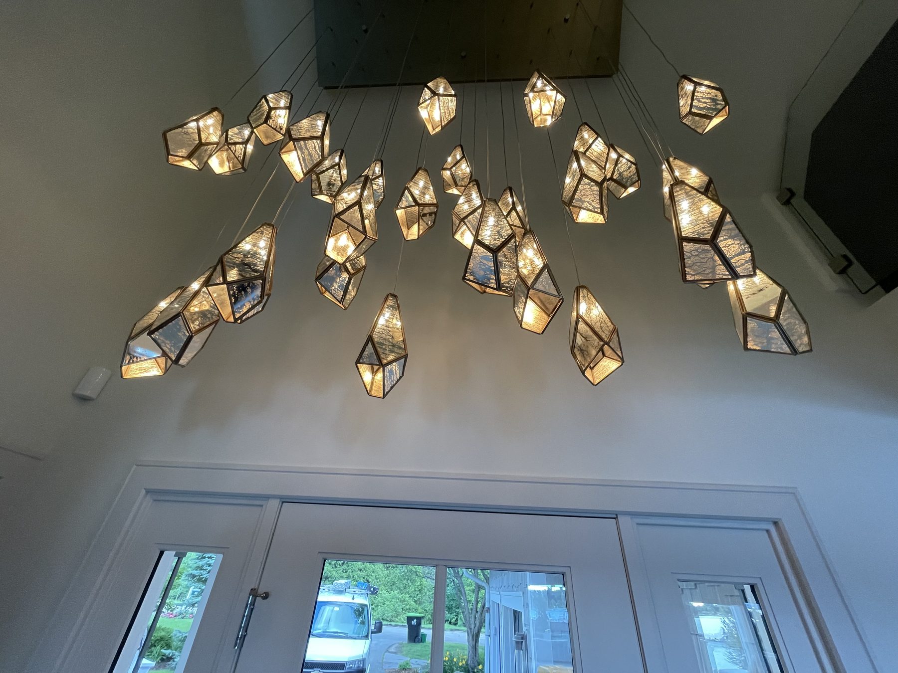 Geometric crystal pendant cluster suspended in a high foyer over white French doors and windows