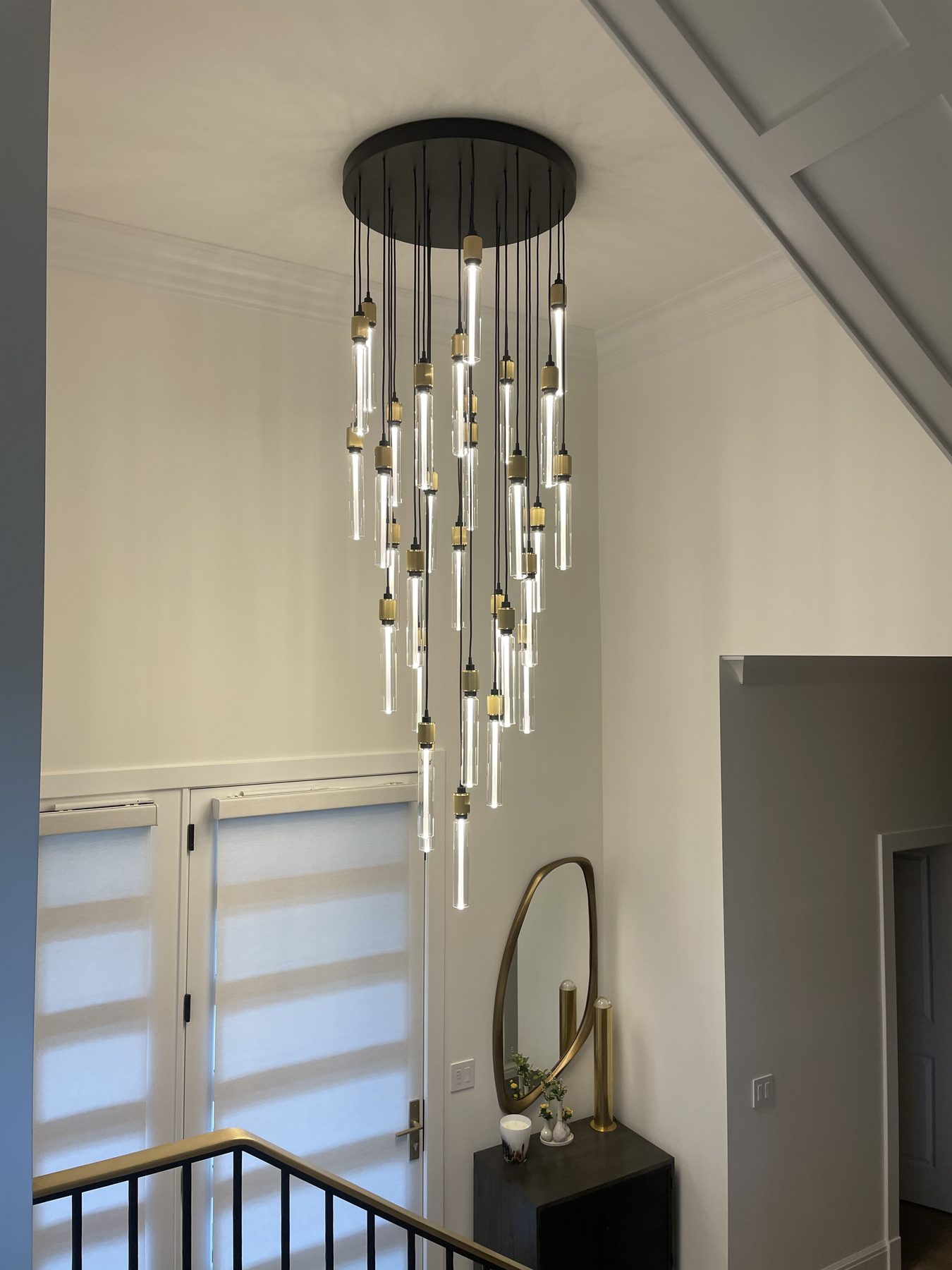 Modern glass-rod chandelier with brass detailing hung over a stairway with brass railing