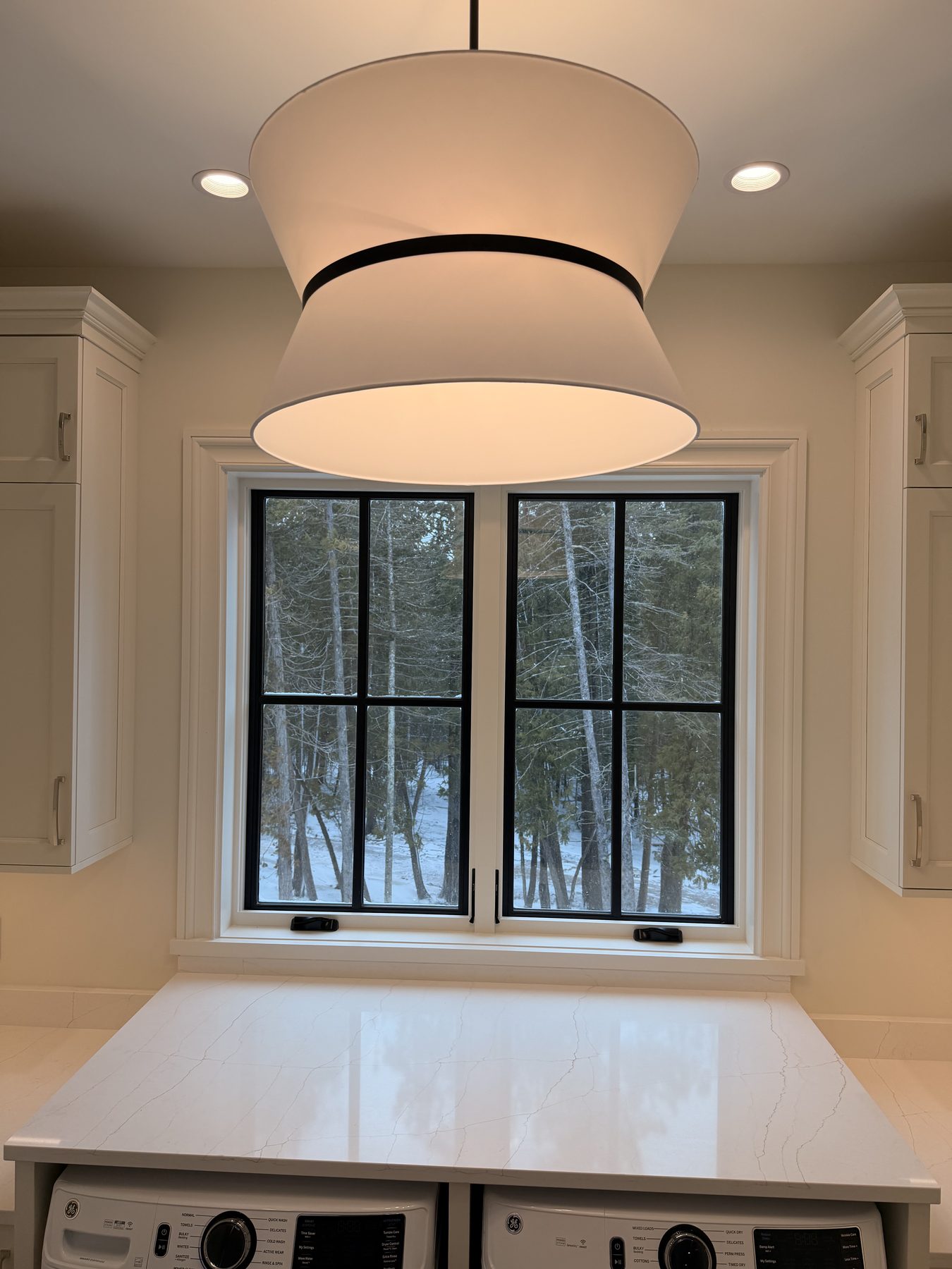 Modern white drum pendant centered over a kitchen island with recessed cans framing it