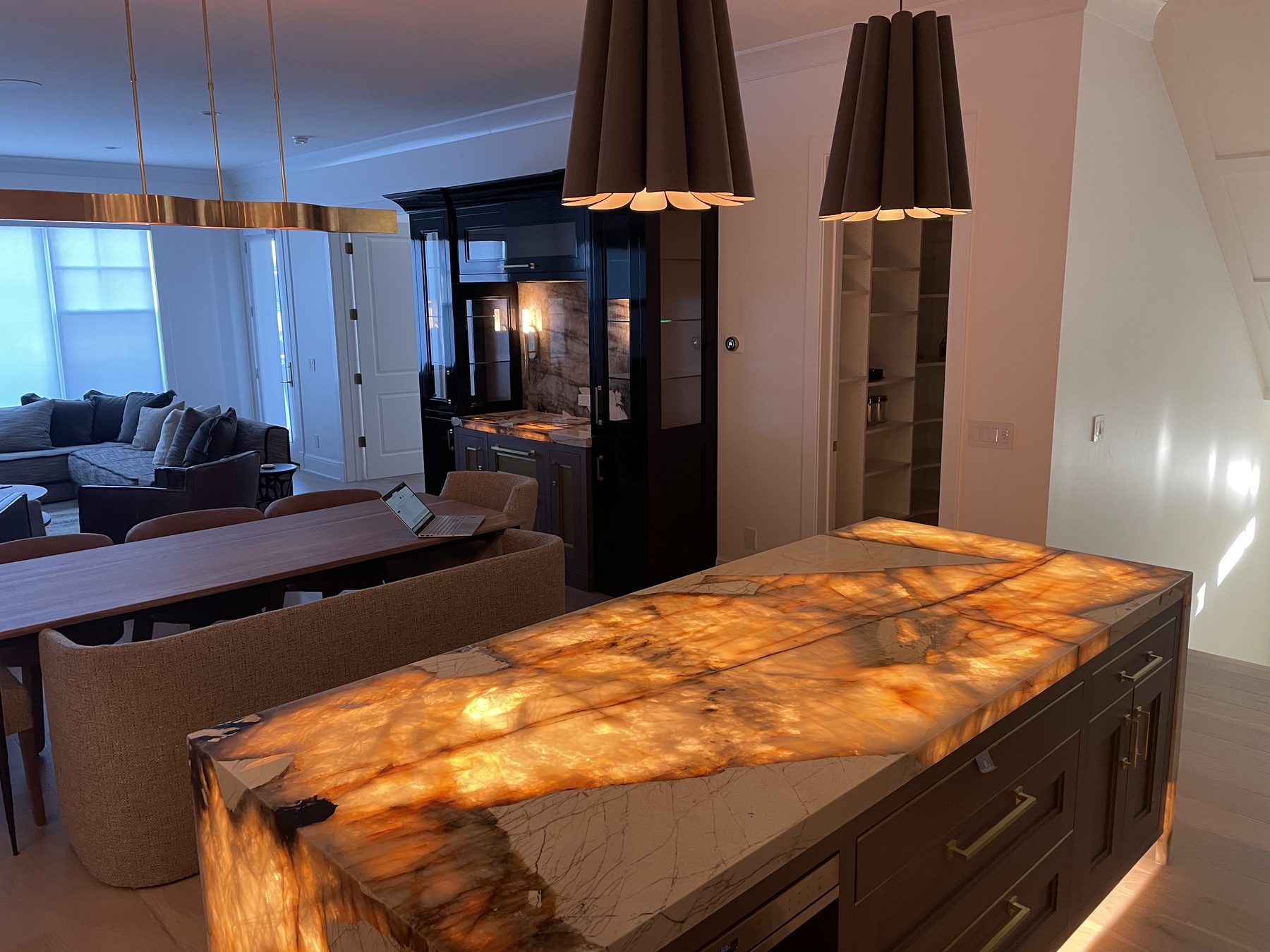 Translucent onyx kitchen island countertop glowing from internal LED backlighting, showing dramatic amber and orange veining through the stone, with cone pendants and dark cabinetry in the dim room