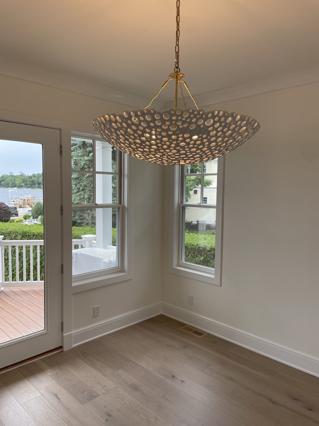 Large organic-textured gold pendant with hundreds of openings hung in a sunlit window-walled foyer with light wood floors